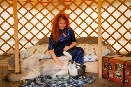 漂亮红头发的女人穿着蓝色蕾丝礼服坐在床上在她的卧室和她最好的朋友玩大狗阿拉斯加