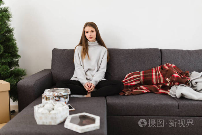 在家里的沙发上坐在毛衣年轻漂亮的女士肖像若有所思地看着相机