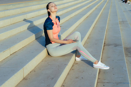 年轻的运动健身女孩在阳光下的台阶上慢跑后休息照片