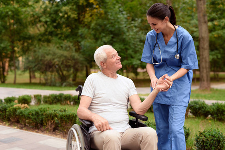 一个护士在一个绿色公园里坐在轮椅上的微笑的老人的脉搏