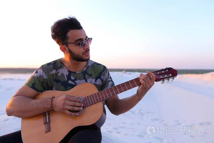 阿拉伯的英俊青年调整吉他，坐在山上的 mi