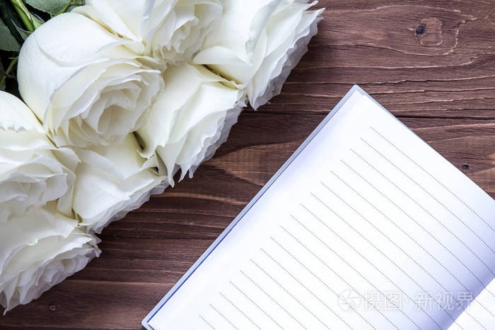 婚礼承蒙笔记本和白玫瑰在木桌上