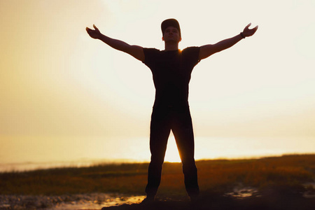 在日落的海面上举起双手的人的剪影照片