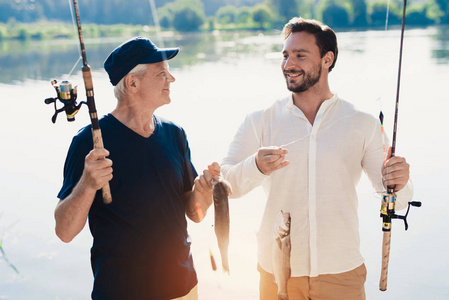 老人和他的成年儿子站在河岸上, 摆着鱼, 他们刚刚抓到