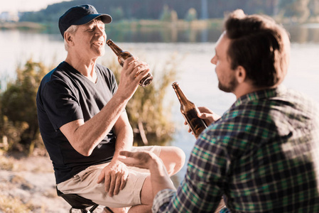 人的休息。一个男人和他年迈的父亲在钓鱼的路上喝啤酒。他们坐在河岸上