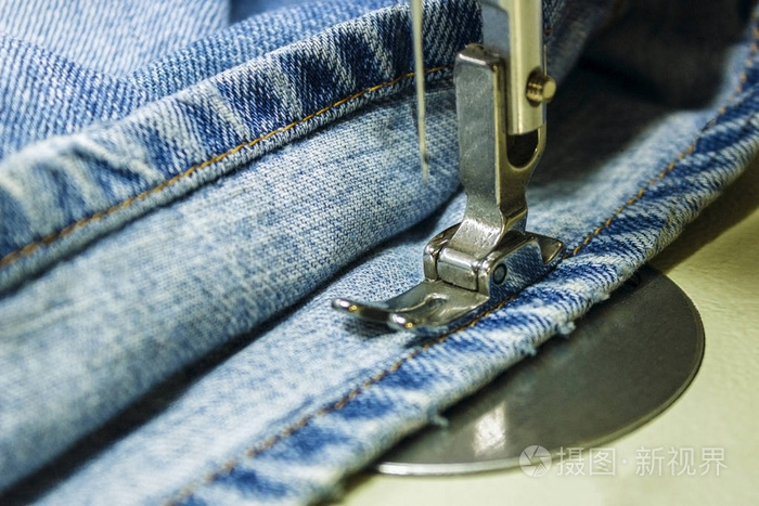 牛仔布在缝纫机上。缝纫的特写