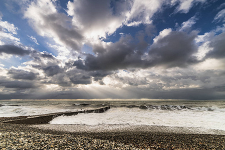 汹涌的海边, 海滩上的鹅卵石, 天空布满了灰云, 太阳几乎是无形的