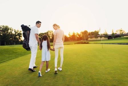 一个男人, 一个女孩和一个女人正在沿着高尔夫球场走向日落, 手牵着手