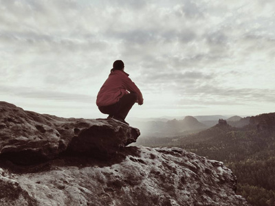 坐在岩石上的徒步旅行者穿红黑色保暖衣的人坐在悬崖上, 欣赏远方的景色