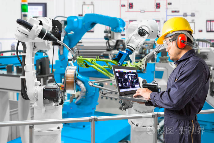 工程师使用笔记本电脑维修自动焊接机器人工件在汽车行业, 智能工厂