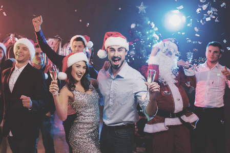 年轻夫妇手里拿着香槟在跳舞。在他们身后舞蹈他们的朋友和男人装扮成圣诞老人