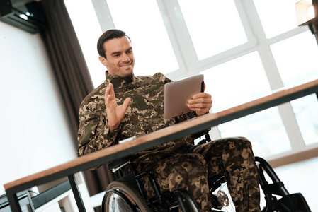 穿着军装的残疾人坐在桌子旁, 与碑一起工作。它后面是一个大的全景窗口
