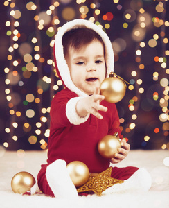 小男孩装扮成圣诞老人玩圣诞装饰, 深色背景照明和博克灯, 冬季假期概念