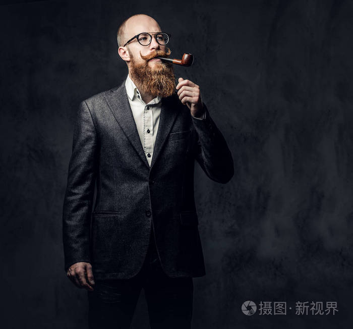红头胡子男性穿着西装和眼镜吸烟传统烟斗在深灰色背景