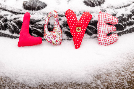 手工字爱雪是由纺织品制成的。明亮的彩色圣诞装饰在雪地上。情人节缝纫玩具