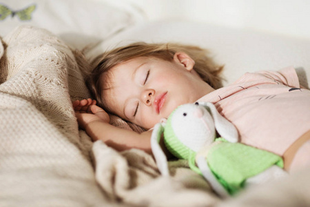 在睡觉的小女孩。无忧无虑的睡眠小宝宝，床上有一个柔软的玩具。针织毛毯上一个美丽的熟睡孩子的特写肖像。甜蜜的梦
