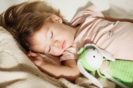 在睡觉的小女孩。无忧无虑的睡眠小宝宝，床上有一个柔软的玩具。针织毛毯上一个美丽的熟睡孩子的特写肖像。甜蜜的梦