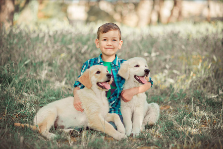逗人喜爱的英俊的男孩与蓝色眼睛玩室外与惊人的白色粉红色拉布拉多猎犬小狗享受夏天晴朗的假日周末与充分的幸福。愉快的微笑的孩子与好朋