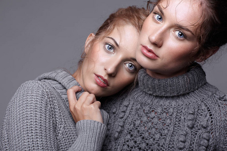 灰色背景的灰色毛衣两个年轻的妇女。美丽的 g