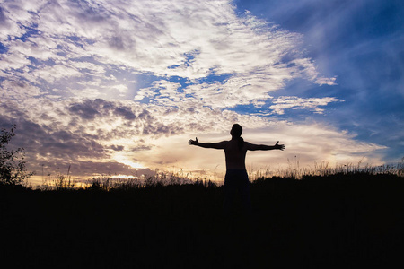 一个人站在田野, 张开双臂迎接太阳的剪影照片