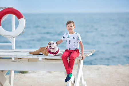 英俊的男孩青少年 happyly 花时间与他的朋友斗牛犬在海边的孩子狗控股玩两个海星接近生活浮标穿红色长裤拖鞋和 tshirt