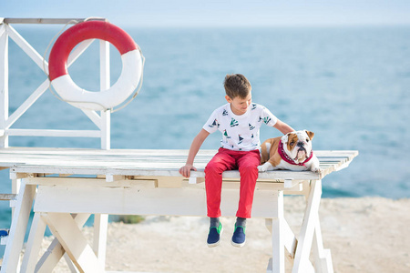 英俊的男孩青少年 happyly 花时间与他的朋友斗牛犬在海边的孩子狗控股玩两个海星接近生活浮标穿红色长裤拖鞋和 tshirt