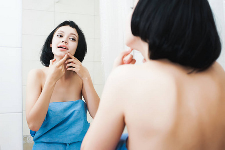 一个黑短发的女人在镜子里看, 挤出粉刺