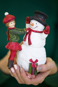 圣诞玩具女孩和雪人在女性手中的绿色背景。圣诞节