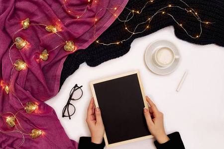 在白色的表面上, 用咖啡杯和其他物品在黑色的小木板上写字的女孩的