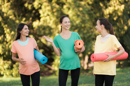 三怀孕的女孩手里拿着瑜伽垫在公园里摆姿势。他们微笑并且有乐趣