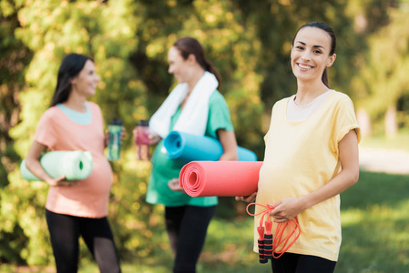 三怀孕的女孩来到公园健身。一个穿着黄色 t恤的女孩, 用毯子做瑜伽和绳子