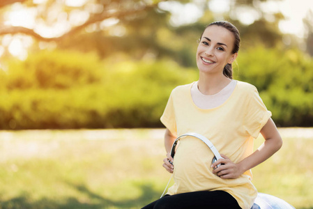 穿着黄色 t恤衫的孕妇坐在瑜伽球上, 听音乐