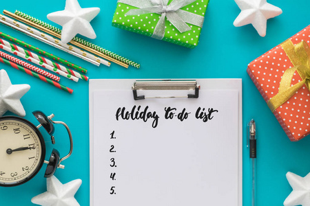 圣诞节和新年假期做列表与记事本, 钢笔, 礼品盒, 时钟, 鸡尾酒管, 在蓝色背景的明星。模仿。平躺, 顶部视图