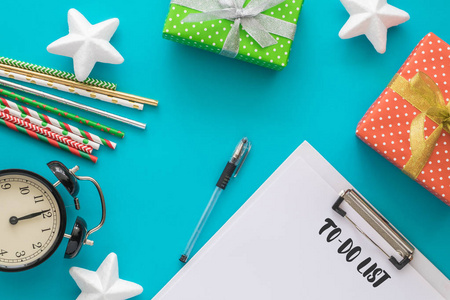 圣诞节和新年假期做列表与记事本, 钢笔, 礼品盒, 时钟, 鸡尾酒管, 在蓝色背景的明星。模仿。平躺, 顶部视图