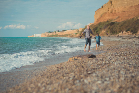 梦幻般的触摸场面英俊的父亲走在海边的石头海滩与可爱的儿子穿着时髦的衣服一起享受夏日时光