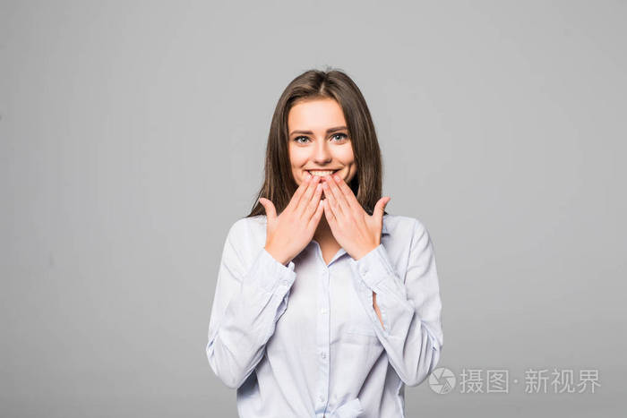 关闭快乐的年轻女子微笑着在相机, 而她的嘴用手捂着灰色的背景