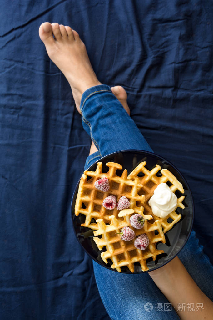 比利时华夫饼配奶油和速冻的树莓女人蓝色陶瓷板s手顶视图