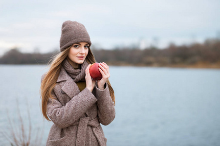 女孩在一个针织帽和围巾与苹果在秋季自然