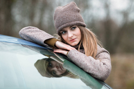 女孩在一个针织帽和围巾附近的汽车在秋季的性质