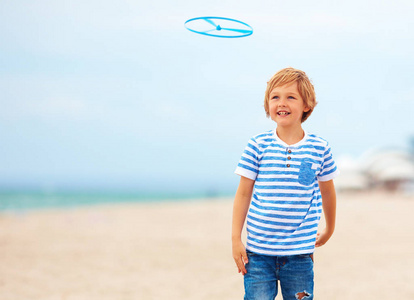 愉快的逗人喜爱的小男孩, 孩子有乐趣在沙滩, 玩休闲活动游戏与螺旋桨玩具