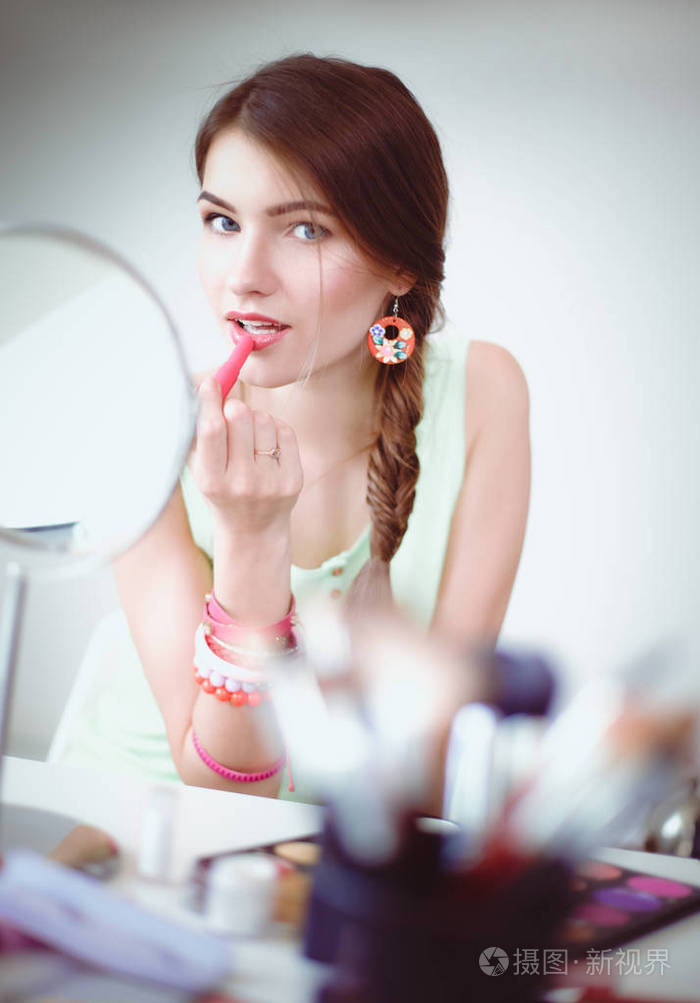 年轻漂亮的女人,使附近镜子,坐在办公桌前的化妆