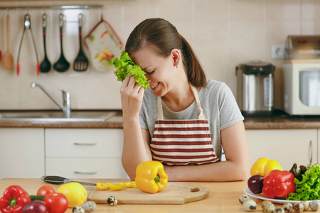 一个年轻漂亮的女人在厨房里笑着生菜叶子的围裙。节食概念。健康的生活方式。在家做饭。准备食物