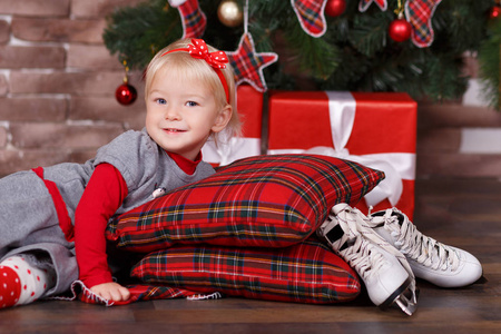 圣诞节美丽可爱的女婴摆在休闲衣服接近新年松树绿树与礼物枕头和玩具马在工作室场景