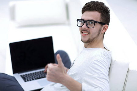 现代年轻的坐在前面的开放式笔记本电脑, 并显示拇指
