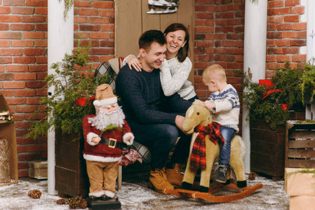 年轻快乐的父母带着一个可爱的小男孩在摇椅上, 穿着毛衣在装修的新年房里与圣诞老人在家里。圣诞节好心情。生活方式, 家庭和假日20