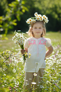 可爱的金发碧眼的年轻女孩穿着白色的衬衫穿着雏菊 chamomiles 在森林野生 mayweed 的草地上摆着花圈。Adorea