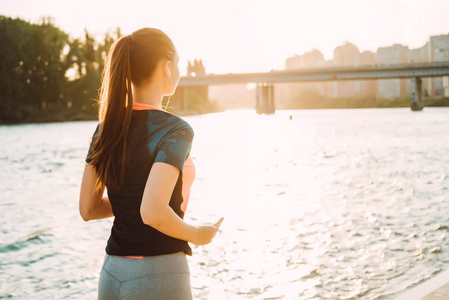 运动长发女孩日落时在河边奔跑, 听耳机上的音乐照片