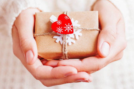 女士在针织毛衣举行新年礼物。礼品包装在工艺纸上, 白色毛毡雪花和红心。Diy 的方式来包装圣诞礼物