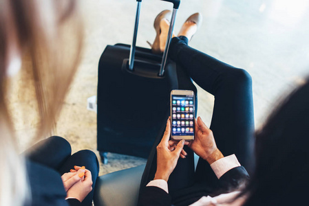 女性手持智能手机与不同应用在屏幕上的特写镜头坐在她的腿上休息在她的手提箱