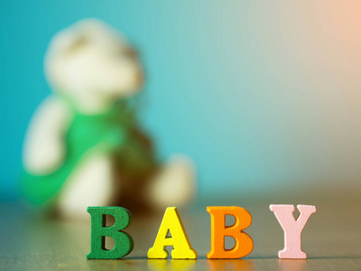 宝贝.英文字母表由木质字母颜色制成。字母表婴孩在木桌和小熊和背景是粉蓝色